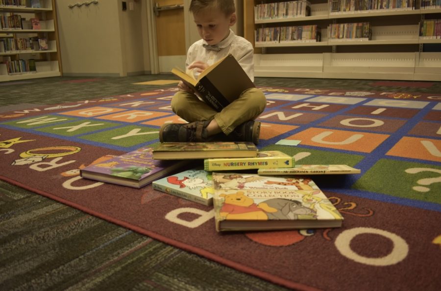 4-year-old Braeden LaDeaux reading To Kill a Mockingbird with childrens books surrounding him. 