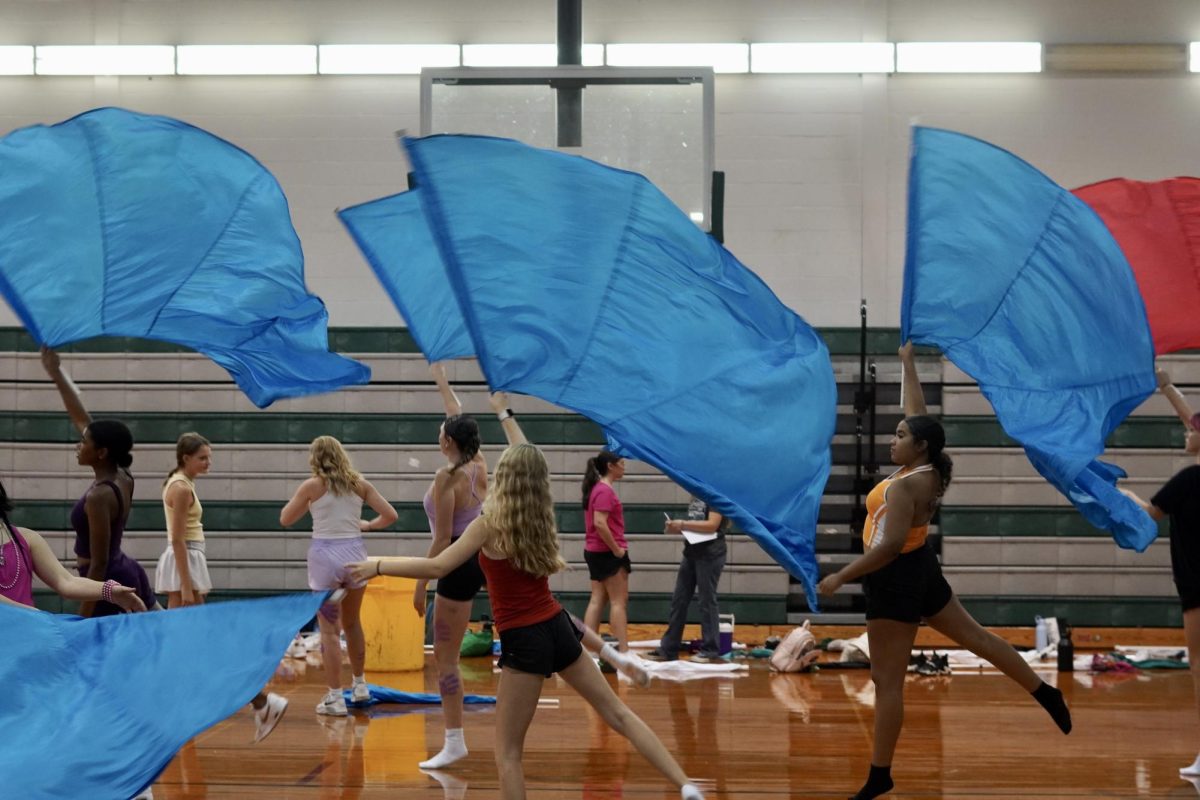 Color guard members practicing their new routine in the small gym with junior color guard captain Shian Fletcher, pictured wearing a purple top and black shorts.