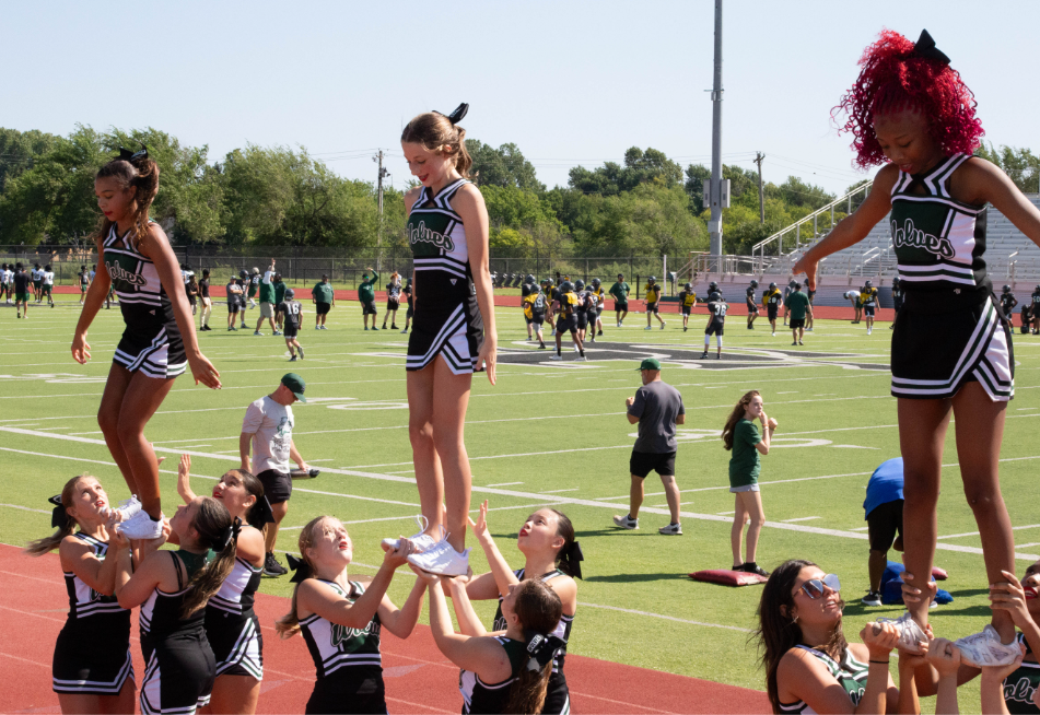 The freshman Cheer team Cheering for the freshman football scrimmage and putting on a show for the people in the crowd.