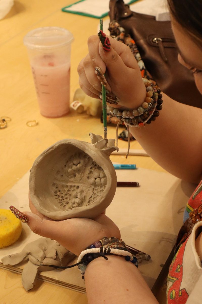 Senior Keely [last name] working on a clay pomegranate dish in ceramics.