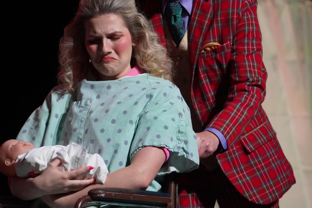 Reese Hollingsworth, as Mrs. Wormwood, looking at her newborn, Matilda, with disgust as junior Easton Hernandez, as Mr. Wormwood, wheels her away.