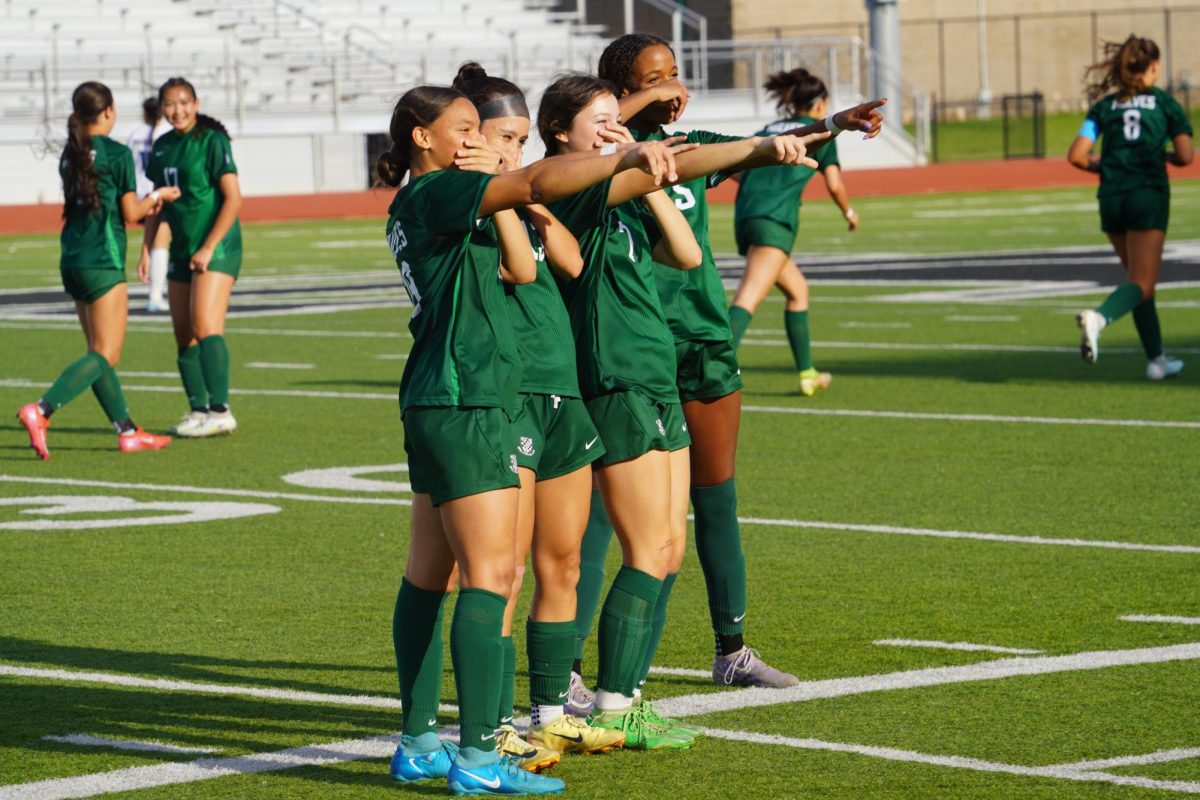 Girls varsity soccer team posing for a photo after scoring a goal.