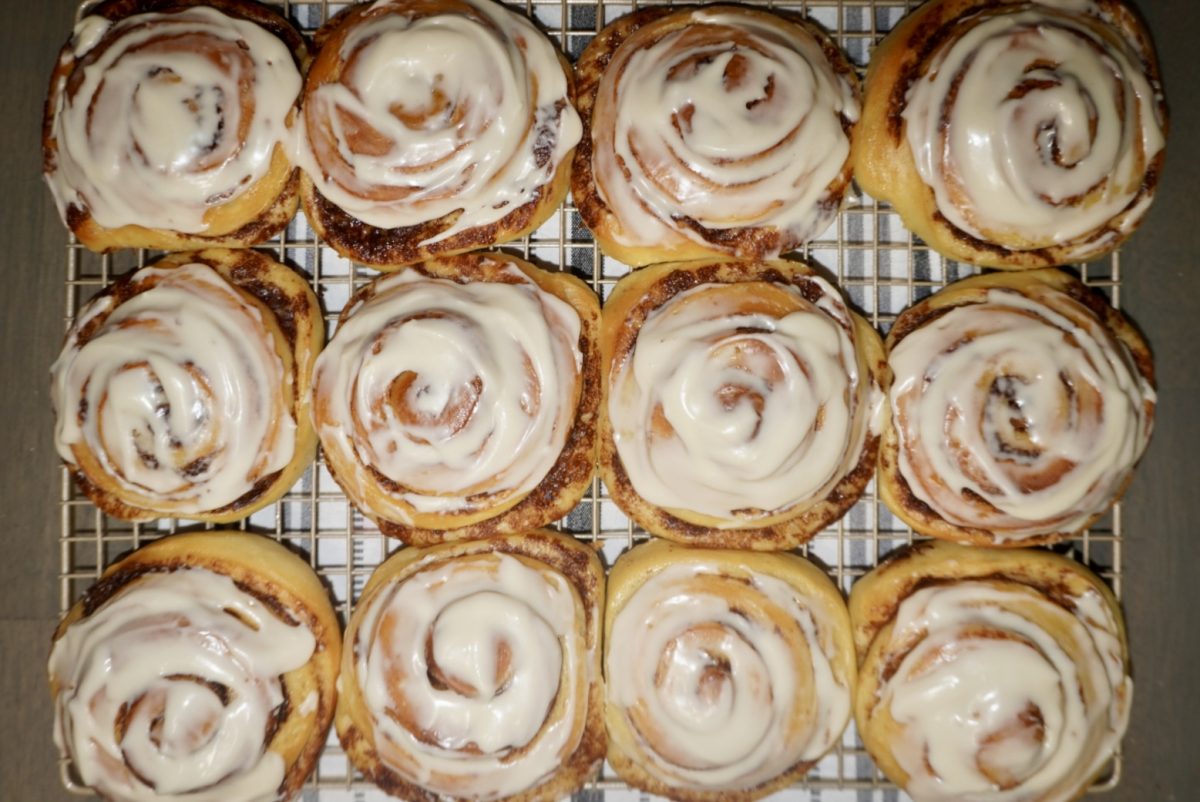 A dozen glazed cinnamon buns on a cooling tray right after being garnished. 