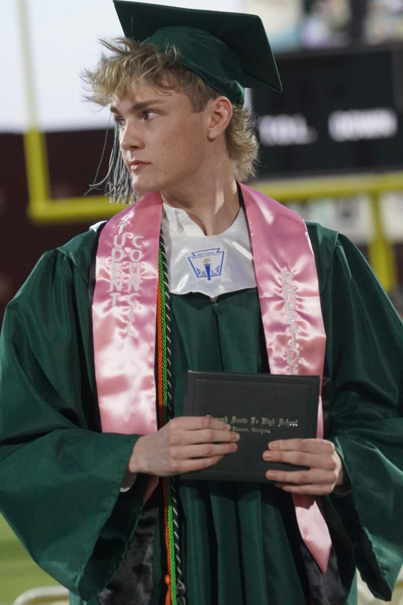 Senior Gabe White looking to the left while holding his high school diploma. 